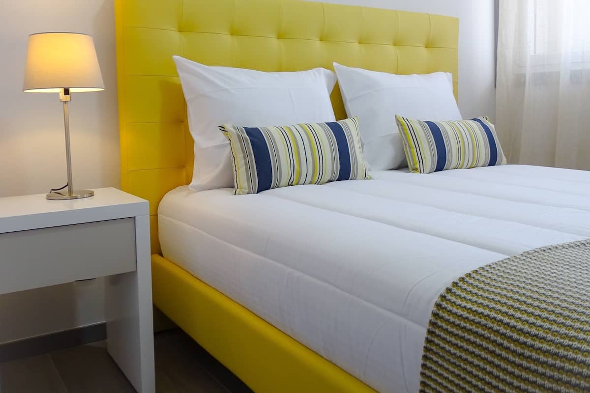 A bed with a yellow headboard, white bedding, and striped pillows.