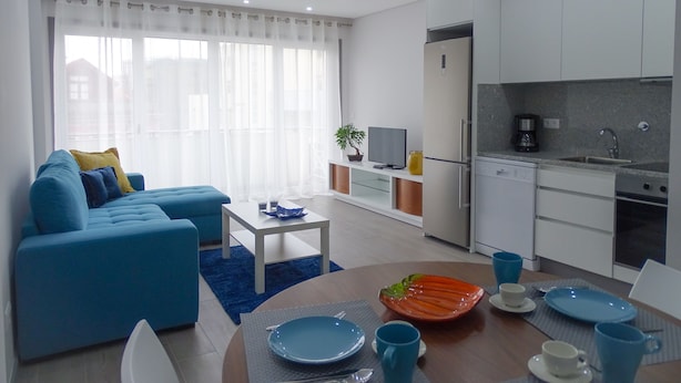 A modern living room with a blue sofa, a coffee table, and a dining area with blue plates and cups. - Rs porto Apartments (Porto)