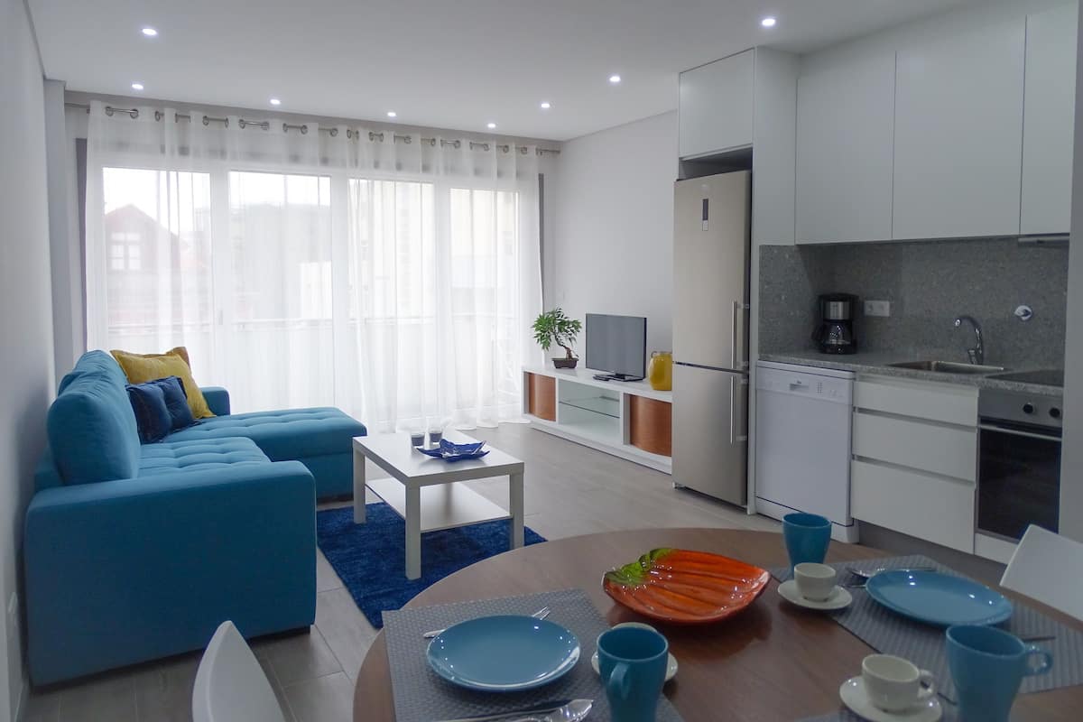 A modern living room with a blue sofa, a coffee table, and a dining area with blue plates and cups.
