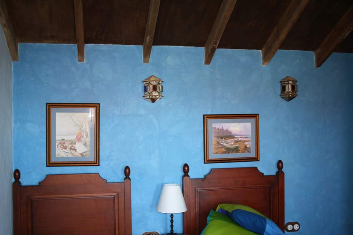 Une chambre à coucher avec un lit en bois, deux lampes fixées au mur et deux tableaux encadrés.
