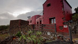 Ein rotes Gebäude mit rustikalem Steinunterbau, Holzzaun und einer Steinmauer.