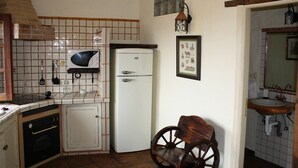 Eine Küche mit Mikrowelle, Kühlschrank, Backofen und einem Holzbstuhl.