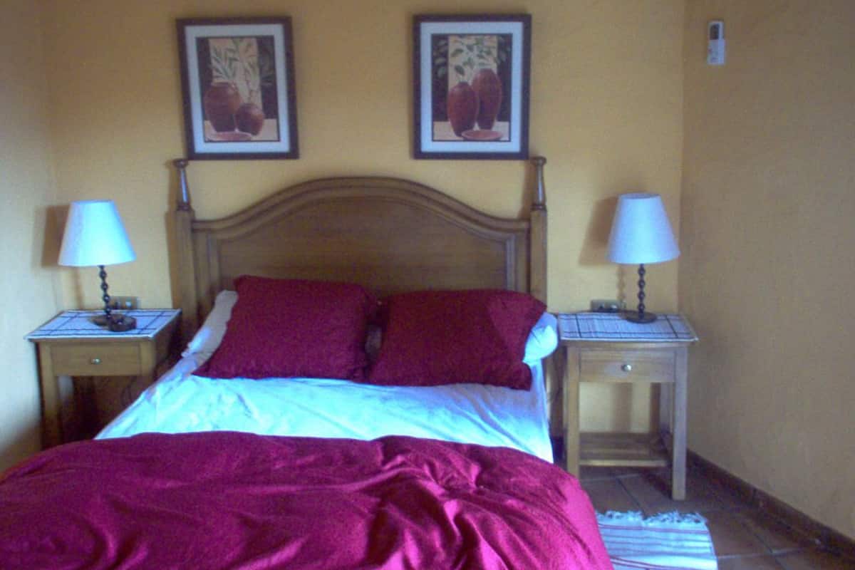 Un lit avec une tête de lit en bois, deux tables de chevet avec des lampes et deux tableaux encadrés accrochés au mur.