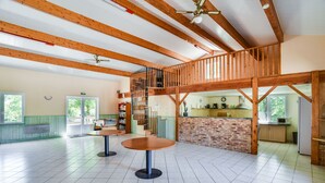 Ein geräumiger Saal mit hohen Decken und freiliegenden Holzbalken, mit einer zentralen Treppe, die in ein Obergeschoss führt.