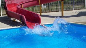 Eine Wasserrutsche in einem Schwimmbecken mit einem Metallzaun im Hintergrund.