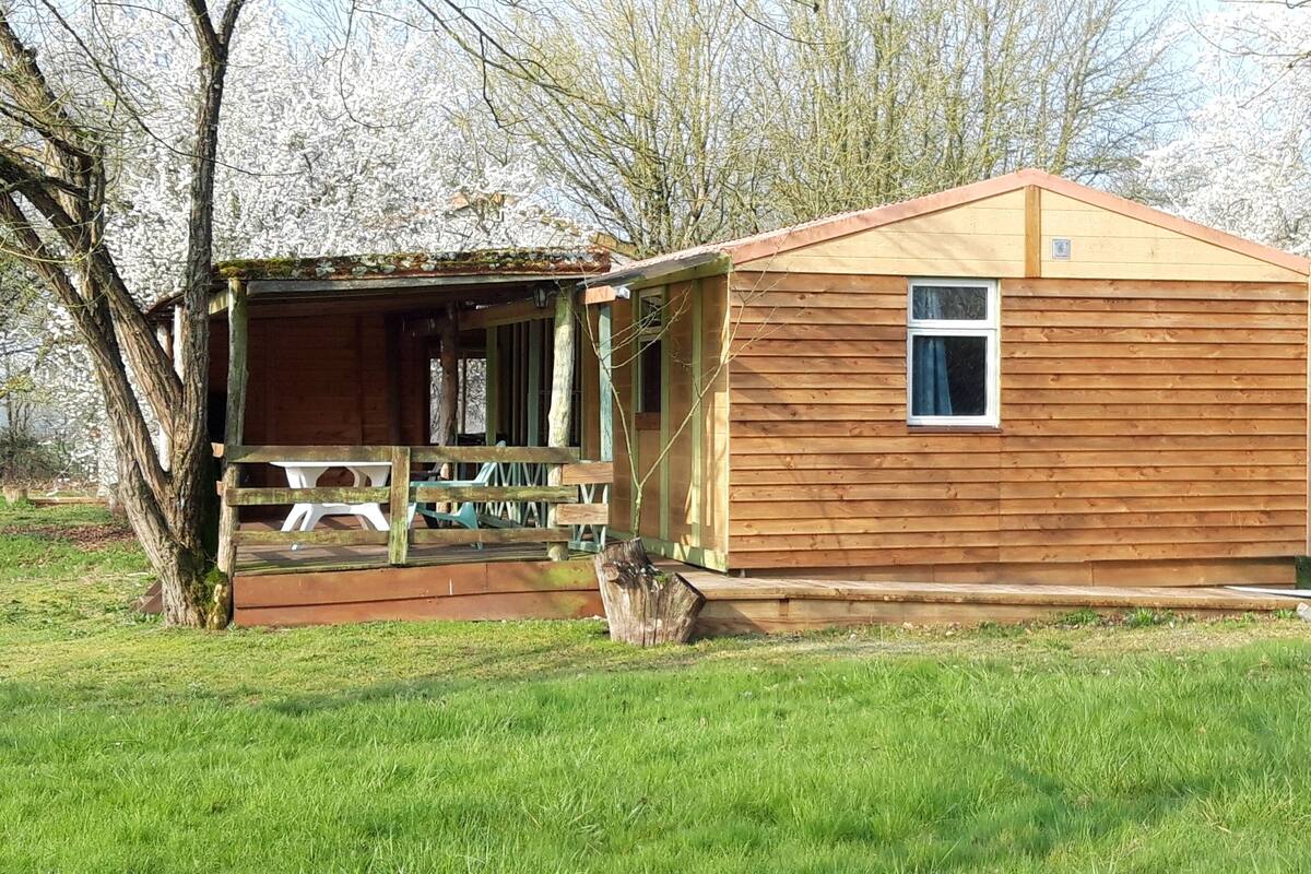 Une petite cabane en bois dotée d’un porche et d’une fenêtre, entourée d’arbres et d’herbe.