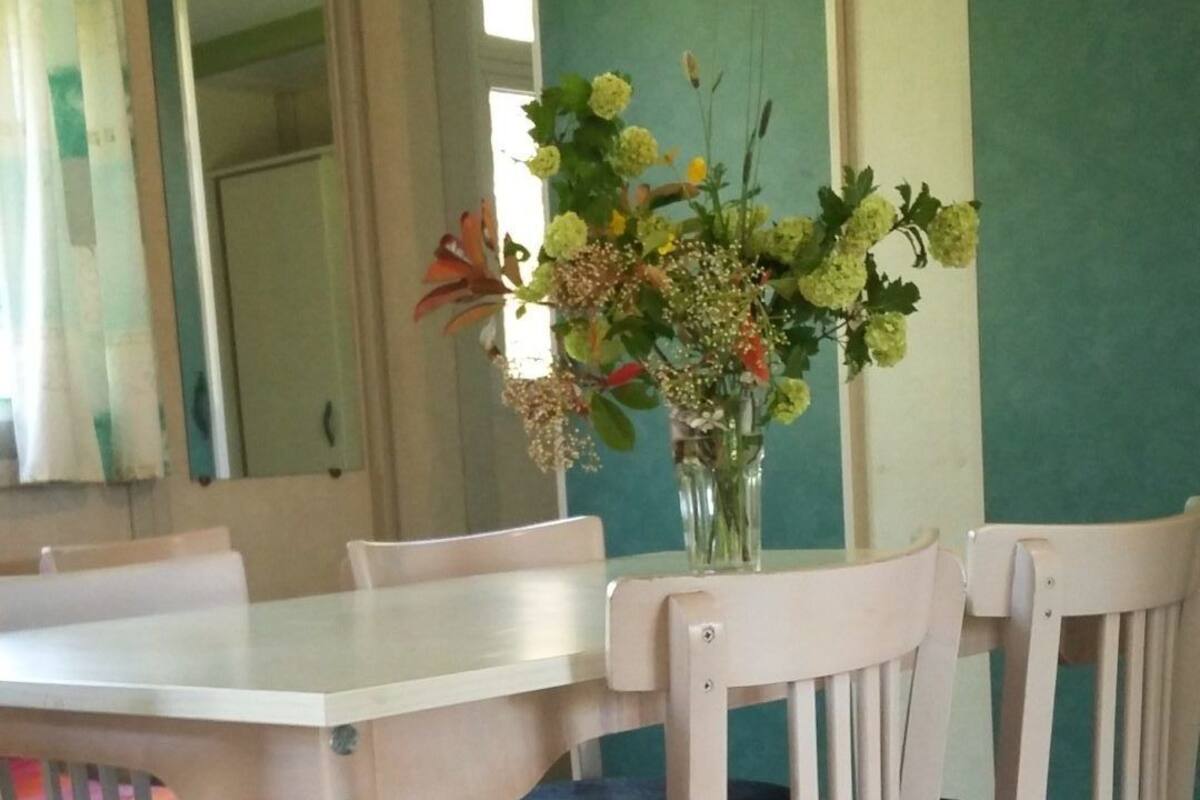 Un coin repas avec une table et des chaises blanches, un vase rempli de fleurs et un mur vert.