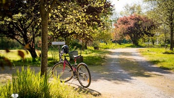 A bicycle parked on a dirt path with a sign reading 'Les Ajoies' in a park setting.
