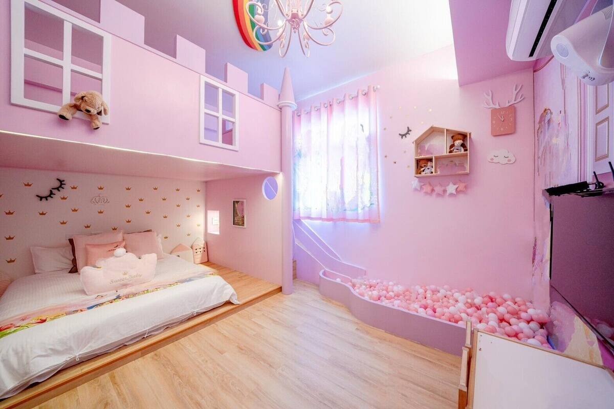 Une chambre à coucher décorée dans des tons de rose, avec un lit, une fenêtre, un ours en peluche, une étagère et une piscine à balles.