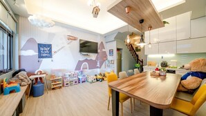 A modern kitchen with white cabinets, a wooden dining table, and a yellow chair. - Yilan 1955 Kids Friendly B&B (Wujie)