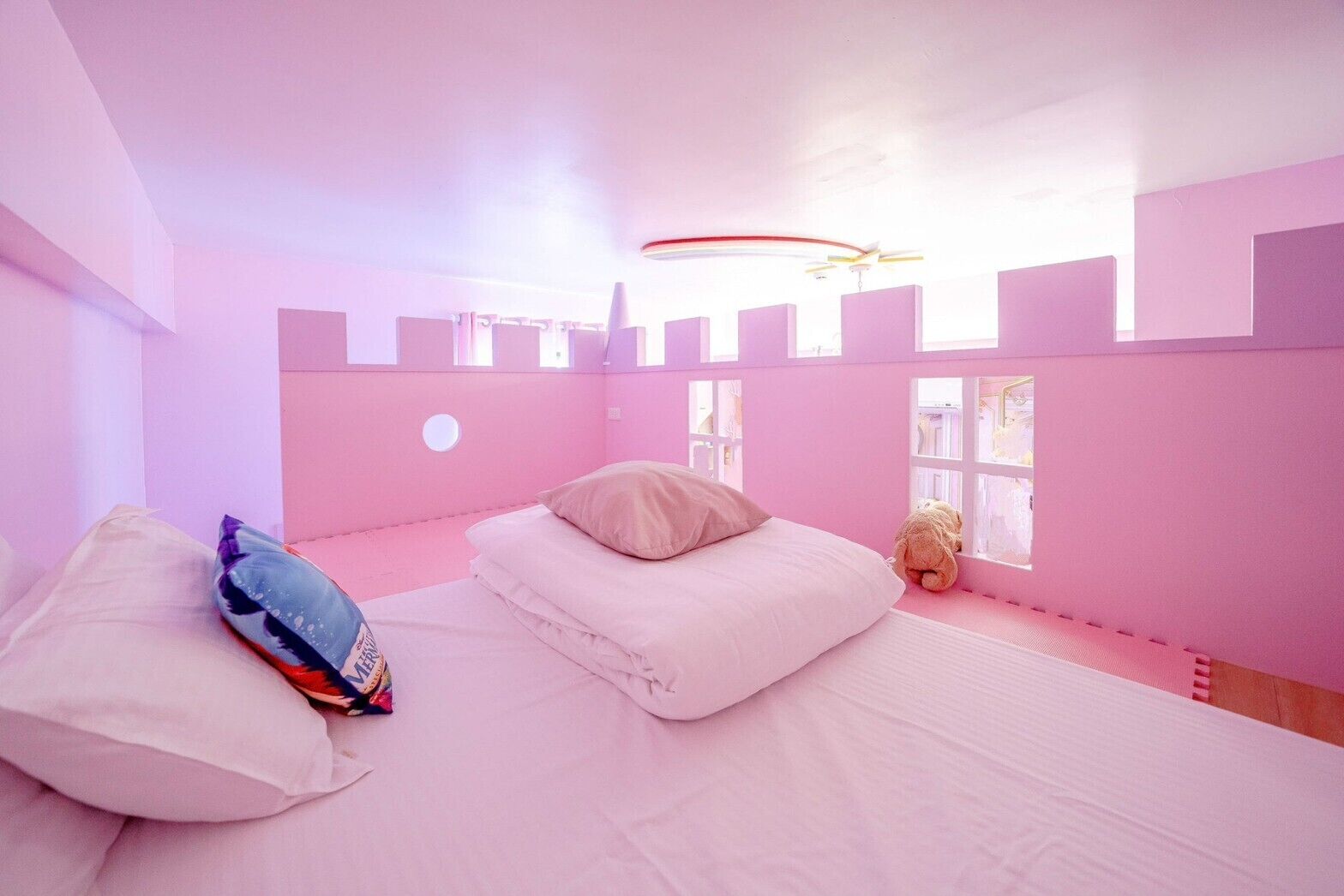 A pink-themed bedroom with a bed, pillows, and a teddy bear.
