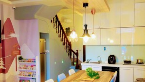 A modern kitchen with white cabinets, a wooden dining table, and hanging pendant lights. - Yilan 1955 Kids Friendly B&B (Wujie)