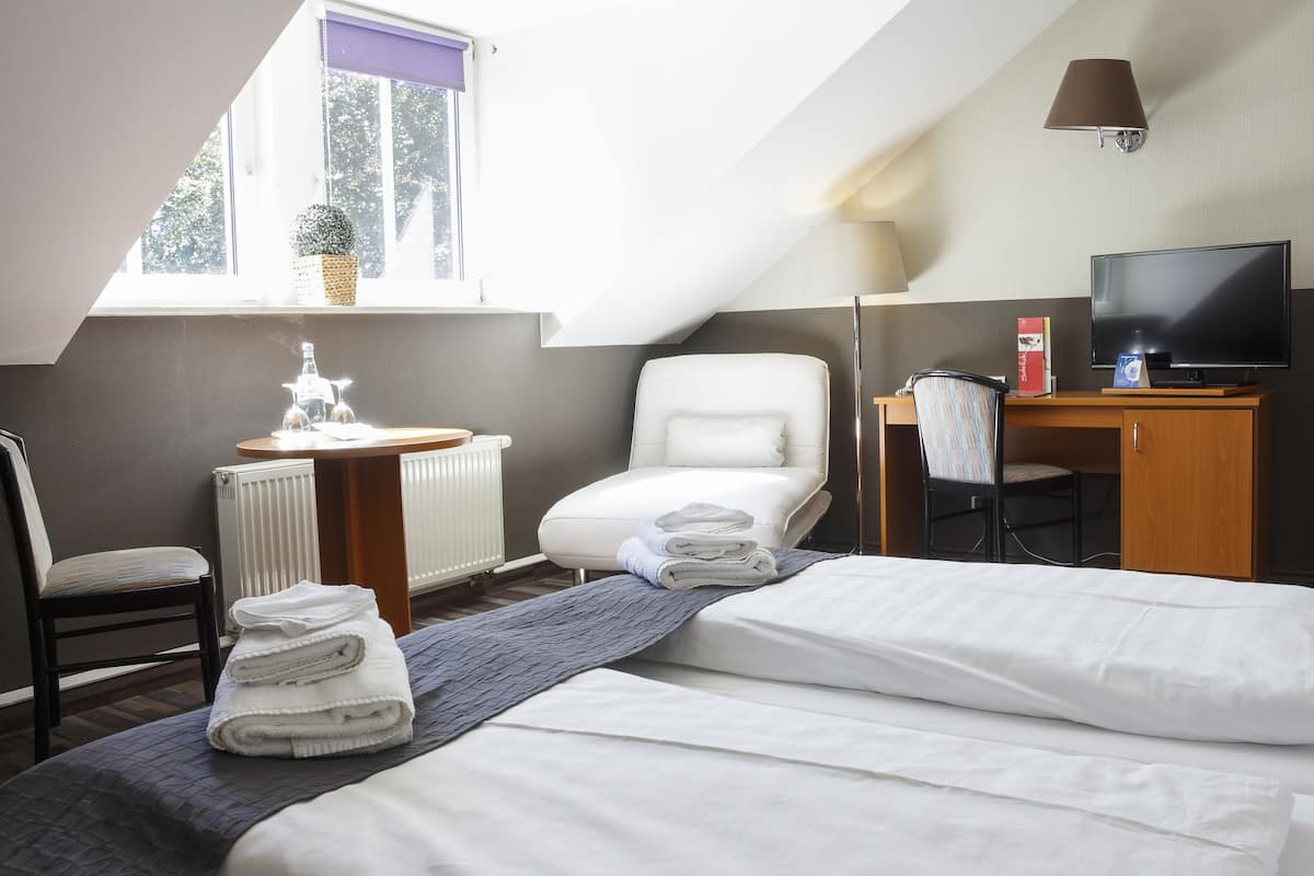 Une chambre d’hôtel avec un lit, une chaise, un bureau avec une télévision et une fenêtre donnant sur des arbres.