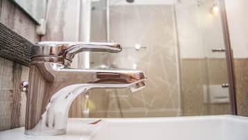 A bathroom with a chrome faucet, a white sink, and a glass shower enclosure.