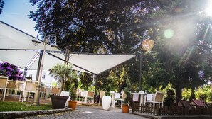 Un patio al aire libre con mesas y sillas, rodeado de árboles y un toldo blanco.