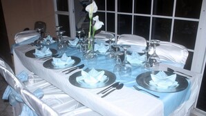 Een lange eettafel, gedekt voor meerdere personen, met borden, bestek en glazen bij elk zitplaats.