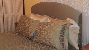A bedroom with a bed, patterned bedding, a wooden wardrobe, and a window with sheer curtains. - Dream Vacation ST Catherine Jamaica - Guest Suites for Rent in Spanish Town (Spanish Town)