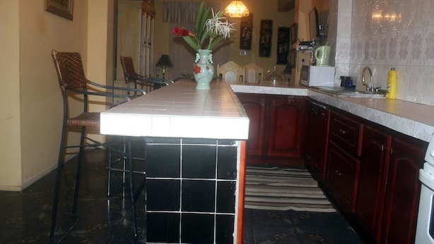A kitchen with a central island, dark floor tiles, and a dining area with chairs. - Dream Vacation ST Catherine Jamaica - Guest Suites for Rent in Spanish Town (Spanish Town)
