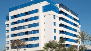 Un hôtel à plusieurs étages, doté d’une façade blanche et de touches de bleu, et dont chaque étage est agrémenté de balcons.