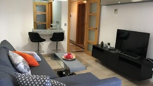 Un salon moderne avec un canapé gris, des fauteuils noirs, une table basse et un téléviseur.