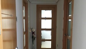 Un couloir avec des portes en bois, un sol carrelé en noir et beige, et un luminaire au plafond.