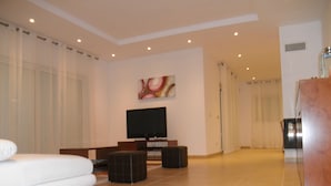A spacious living room with a large flat-screen TV, a white sofa, and a wooden coffee table. - Villa 3 luxury Suites with Pool (loulé)