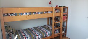 Uma cama beliche com colcha estampada e uma estante com livros e uma luminária.