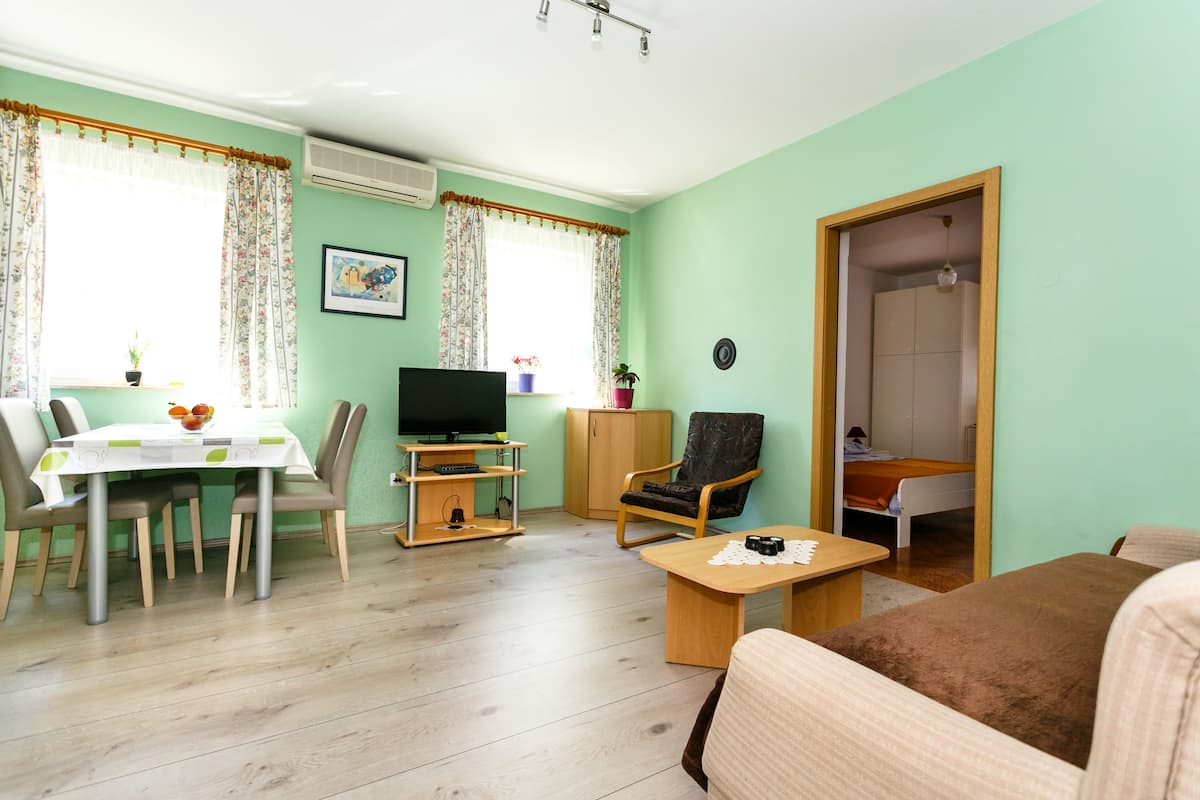 Una sala de estar con una mesa de comedor, sillas, un televisor, un sofá y una pequeña mesa con un objeto decorativo.