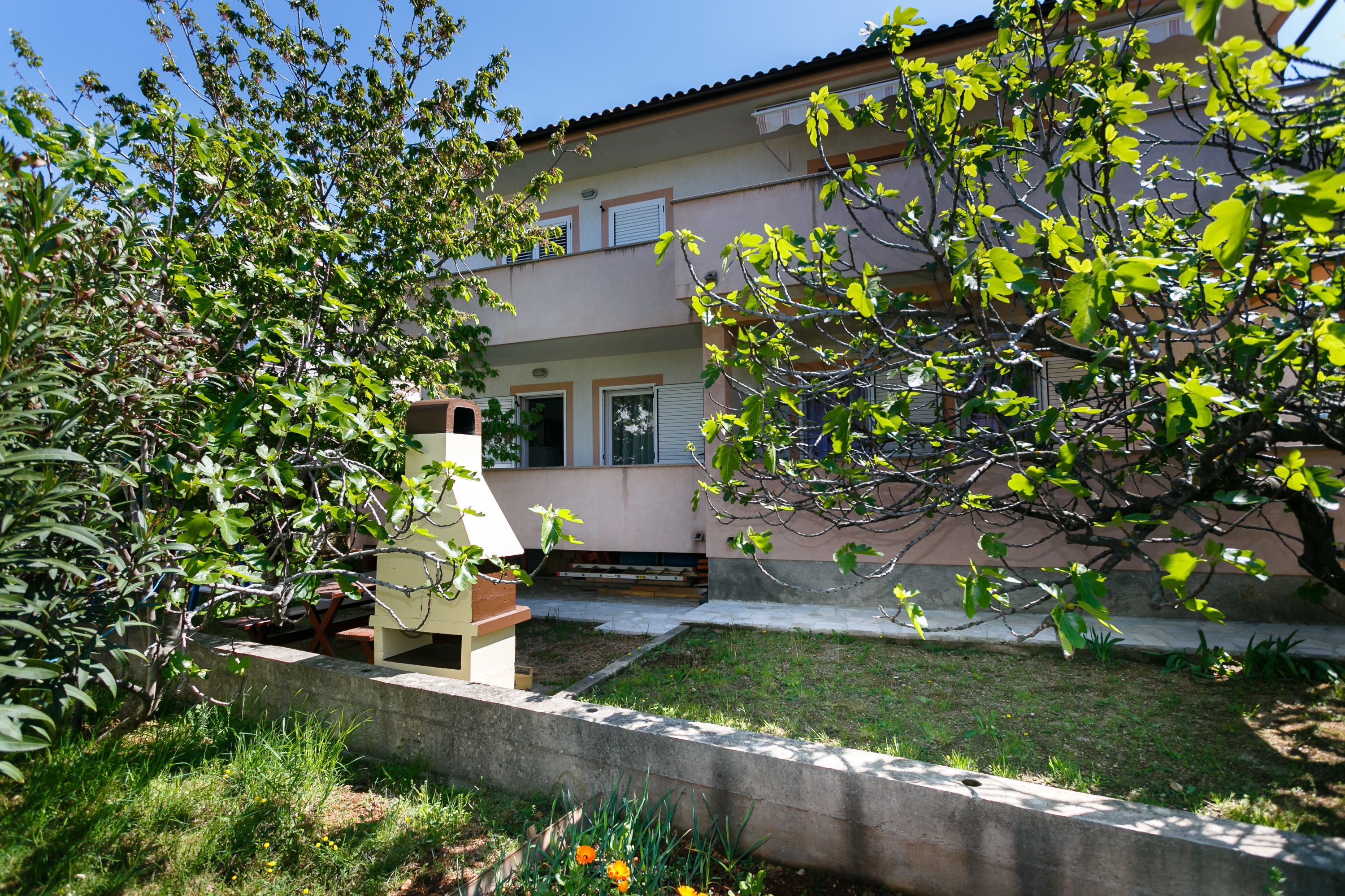 A two-story building with a garden in front, a small outdoor seating area, and a clear sky.