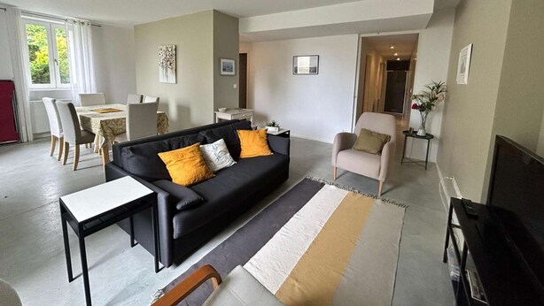 A modern living room with a black sofa, a dining table, and a TV.
