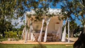 A covered outdoor area with a table and chairs, surrounded by trees and a clear sky. - Casa Kairos (Ostuni)