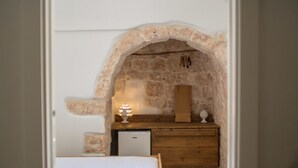 A bedroom with a stone archway, a wooden bed, a nightstand, and a dresser. - Casa Kairos (Ostuni)