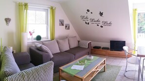 Een gezellige woonkamer met een bank, gestreepte fauteuils, een houten salontafel en een televisie.