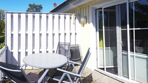 Een terras met een tafel en stoelen, een wit hek en een schuifdeur van glas.