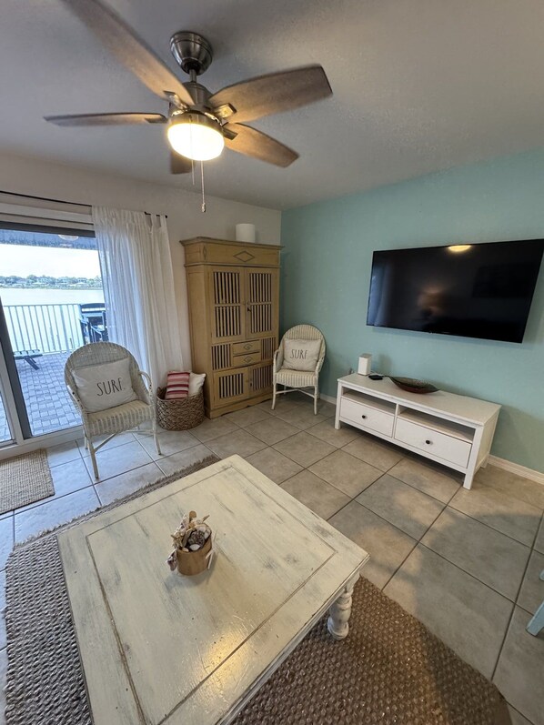A living room with a ceiling fan, a television, a white coffee table, and a view of the outdoors.