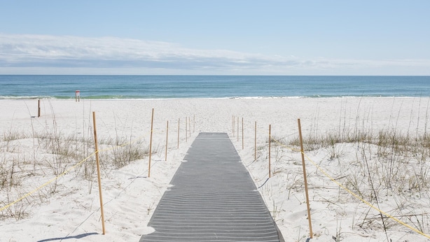 Ein hölzerner Steg führt zu einem Strand mit blauem Himmel.