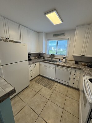 A kitchen with white cabinets, a built-in dishwasher, and a window with blinds.