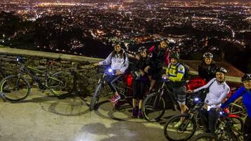 Un groupe de personnes se trouve sur un chemin de pierre, à vélo, et surplombe une ville illuminée la nuit.