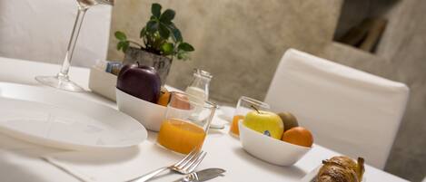 Une table blanche dressée pour le petit-déjeuner, avec un verre de jus d’orange, un bol de fruits, un croissant et un verre de lait.