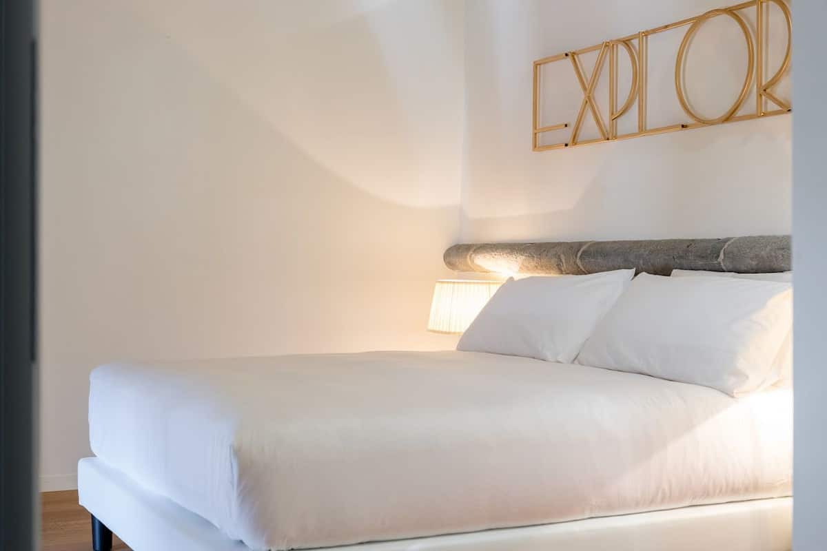 A modern bedroom with a wooden ceiling, a bed with white bedding, and a wall-mounted sign that reads "EXPLORER".