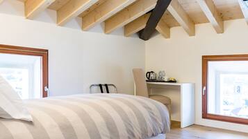 A bedroom with a bed, a chair, a desk with a kettle, and a window.