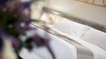 Een keurig opgemaakt bed met witte lakens en een grijs-wit gestreept kussen.