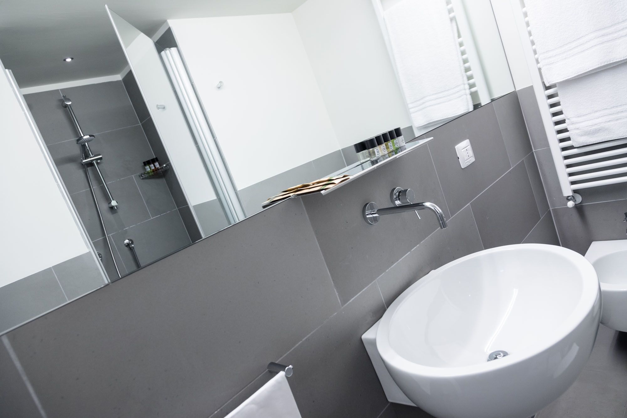 A modern bathroom with a large mirror, a white sink, and a shower area.