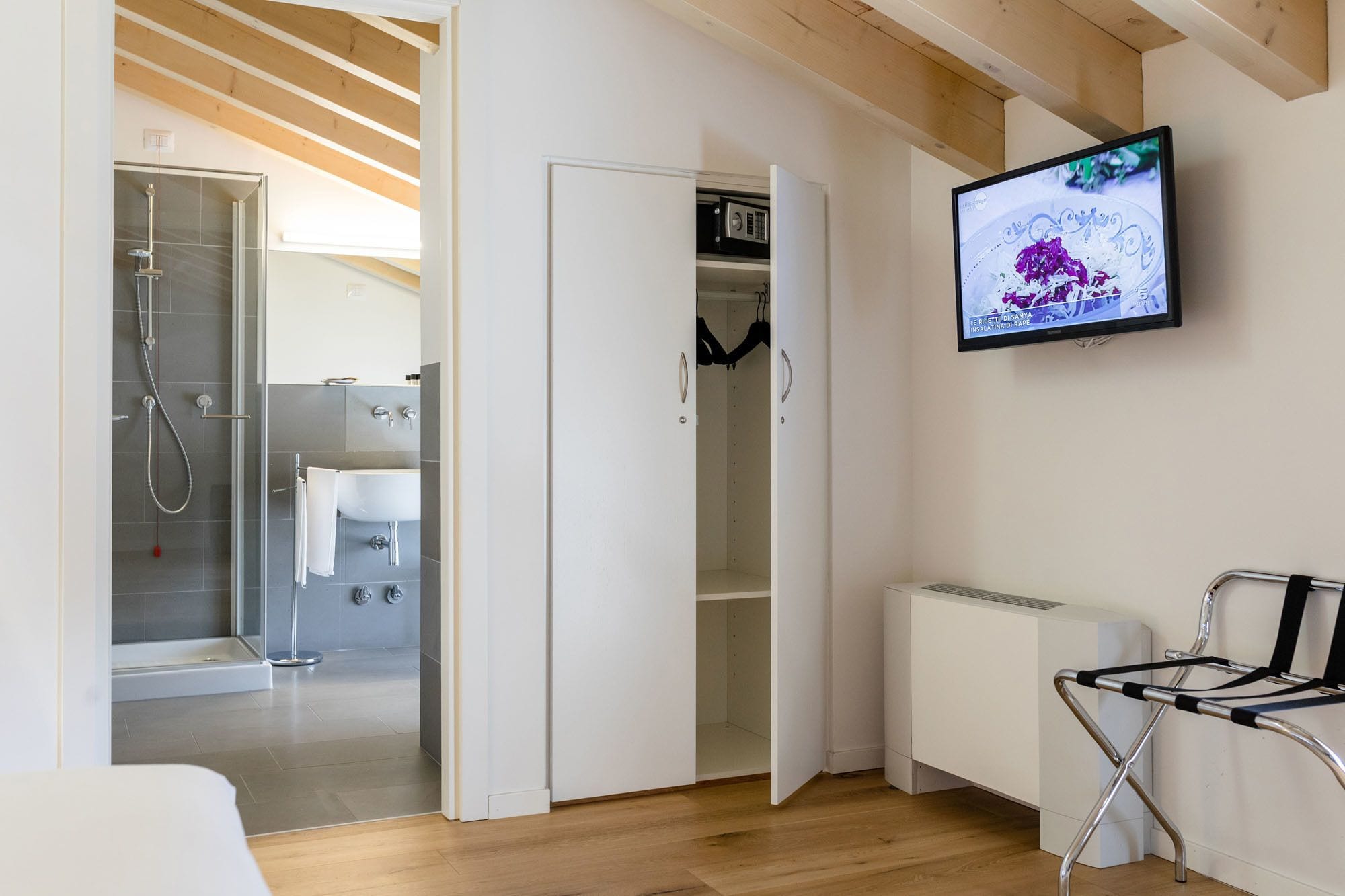 Un baño moderno con ducha, inodoro y lavabo. Un televisor está montado en la pared, y se ve un radiador.