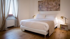 Ein Schlafzimmer mit einem Bett, zwei Nachttischlampen, einem Fenster mit Vorhängen und einem Bild an der Wand.