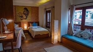 Ein Hotelzimmer mit Holzboden, zwei Betten, einem Schreibtisch mit Stuhl, einem Bild an der Wand und Blick auf Gebäude durch das Fenster.