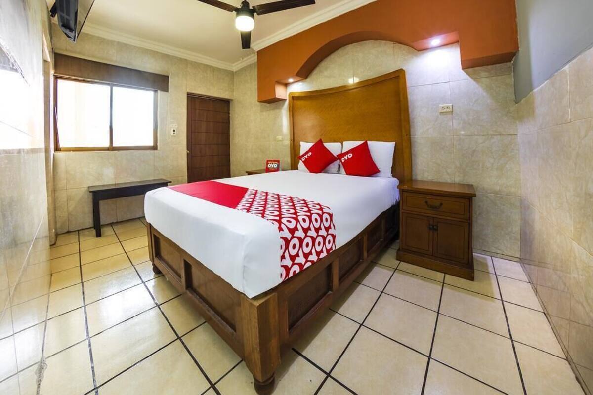 A hotel room with a large bed, a wooden headboard, a bedside table, and a bench.