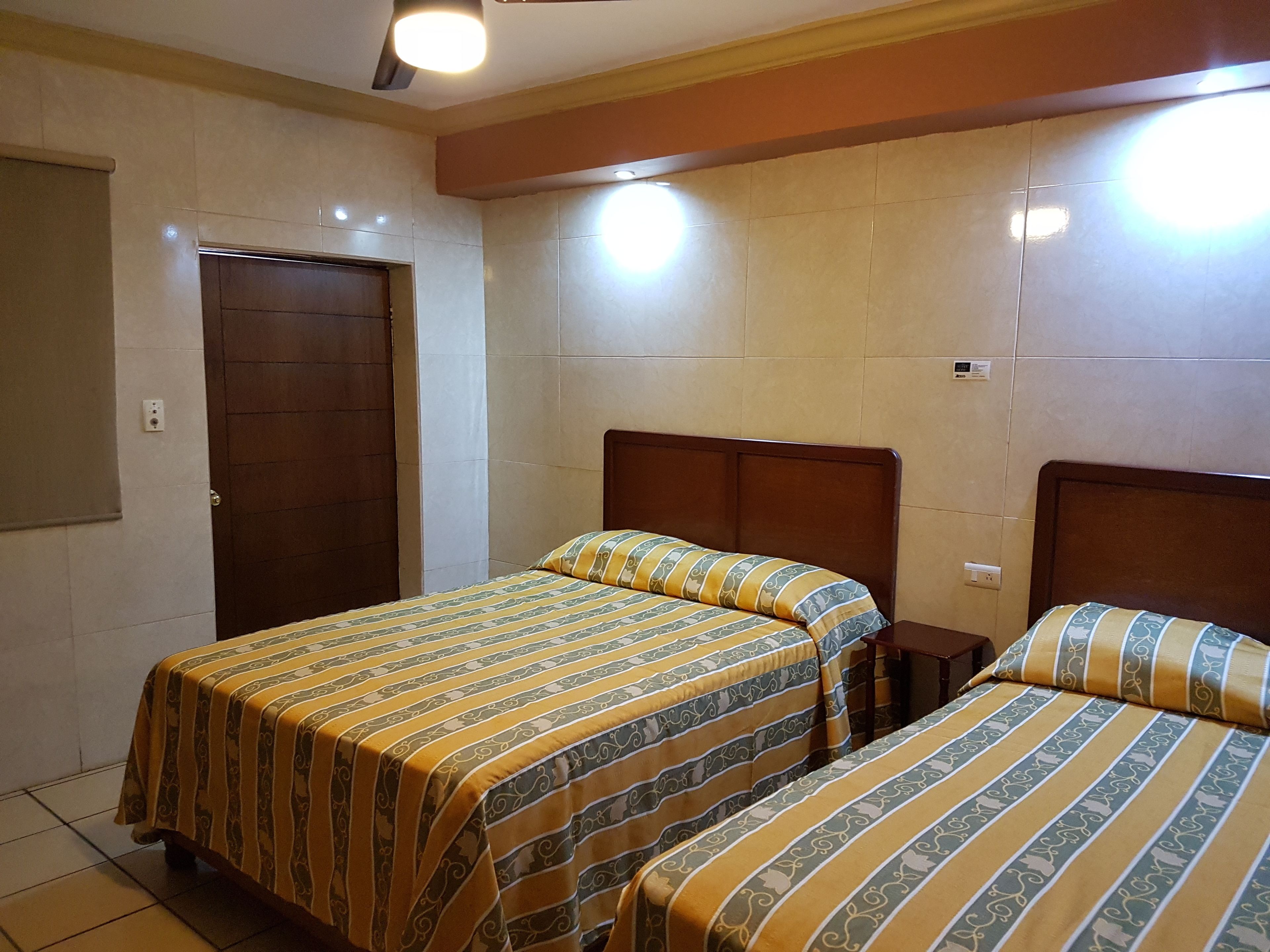 Habitación de hotel con dos camas, una puerta de madera y paredes con baldosas.