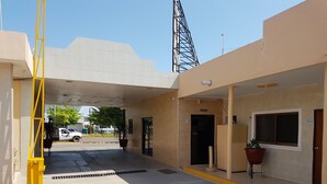 Entrada de hotel com balcão de recepção, placa indicando a recepção e área de estacionamento com barreira amarela.