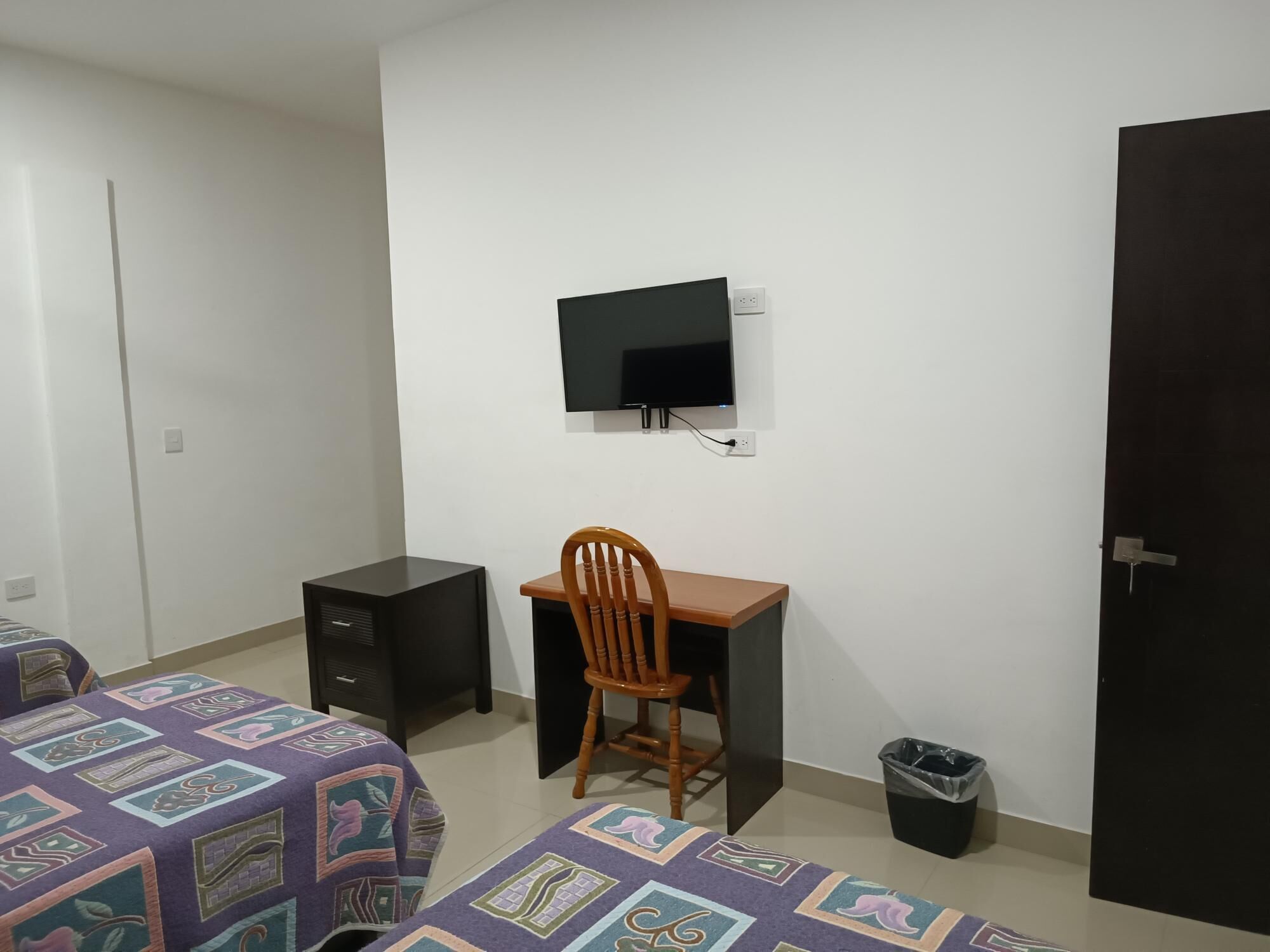 Een slaapkamer met een bed, een bureau, een stoel, een televisie en een prullenbak.